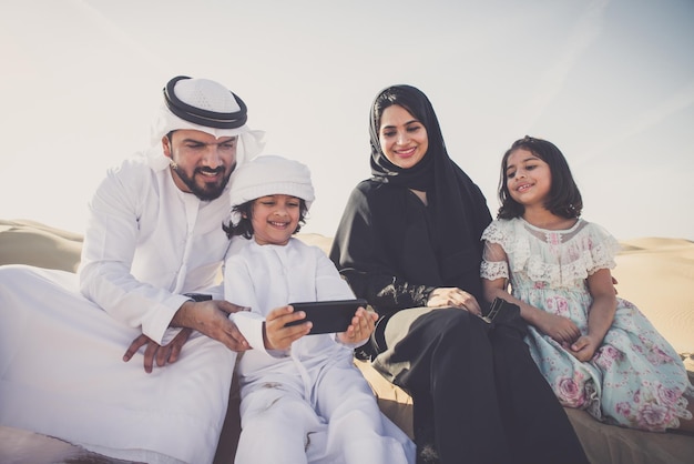 Une famille arabe se fait un selfie assise dans le désert contre le ciel.