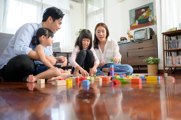 Famille asiatique avec des enfants jouant et construisant une tour de blocs de jouets en bois colorés