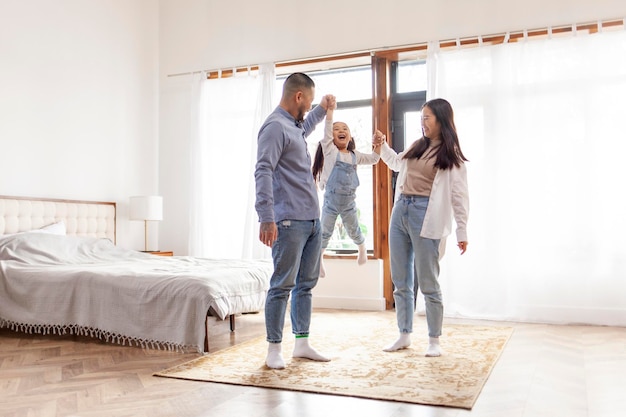 Une famille asiatique heureuse avec une petite fille se tient à la maison dans la chambre à coucher et se réjouit