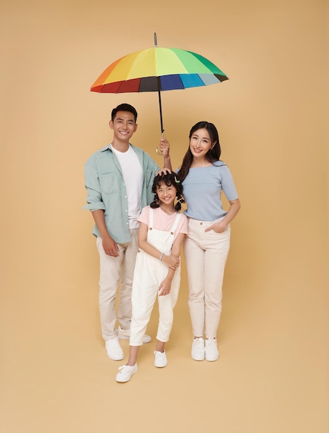 Une famille asiatique heureuse sous un grand parapluie coloré isolée sur un fond de couleur nu