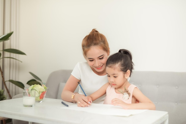 La famille asiatique avec la mère et les filles dessinent sur le papier à la maison