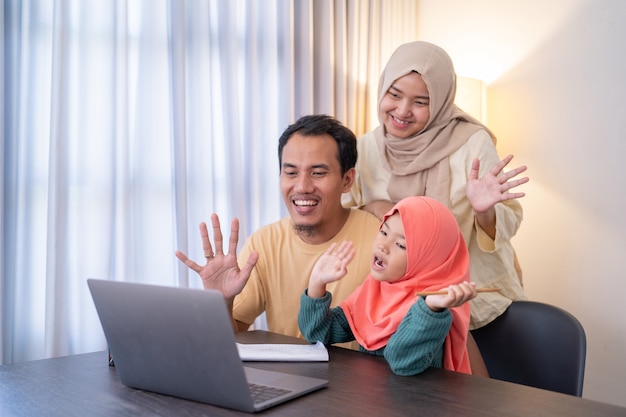 Une famille asiatique musulmane agite la main lors d'un appel vidéo à l'aide d'une tablette avec un ami