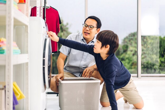 Famille asiatique père et enfant petit garçon fils s'amusant à faire des tâches ménagères faisant la lessive des vêtements sales dans la machine à laver ensemble dans la buanderie à la maison