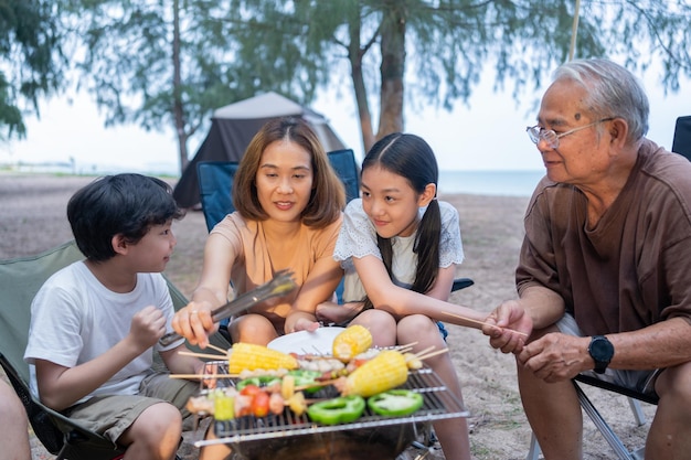 Famille asiatique avec personnes âgées buvant et faisant un barbecue ensemble. Cuisiner un barbecue grillé pour le dîner pendant le camping le doliday d'été.