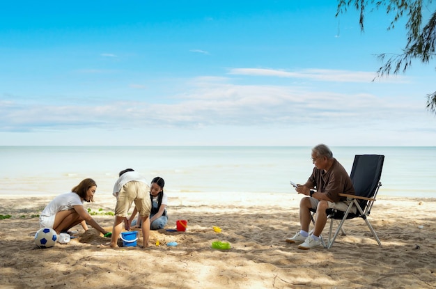 Famille asiatique avec personnes âgées et enfants se relaxant et campant sur une plage tropicale pendant les vacances d'été. Ensemble et mode de vie d'activités de plein air.