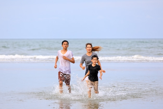 Famille asiatique de trois personnes jouant ensemble sur une plage tropicale avec un ciel bleu en arrière-plan