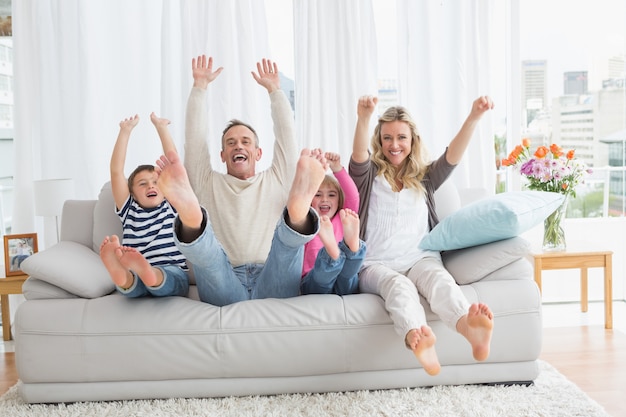 Famille assis sur un canapé et levant les bras