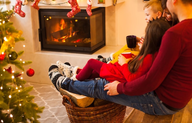 Famille assise sur la branche et se réchauffer le pied près de la cheminée. Temps de Noël, temps en famille avec des tasses de chocolat chaud ou de thé