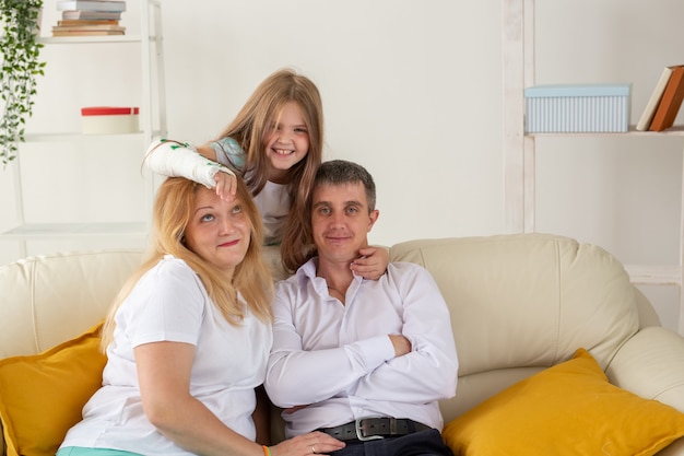 Une famille assise sur un canapé dans son salon a une blessure à la main mais elle est heureuse d'être ensemble