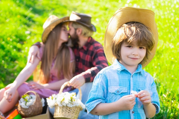 Famille assise sur la pelouse pique-nique dans le parc Garçon souriant avec mère baiser père un jour d'automne Été ensemble concept de loisirs familiaux