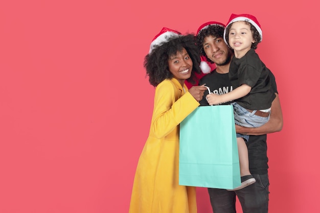 Famille aux cheveux bouclés posant avec un sac bleu et des chapeaux de Noël modelant sur un fond rose