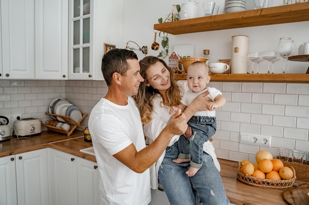 une famille avec un bébé en jeans et T-shirts blancs joue dans la cuisine