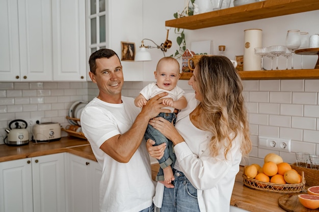 une famille avec un bébé en jeans et T-shirts blancs joue dans la cuisine