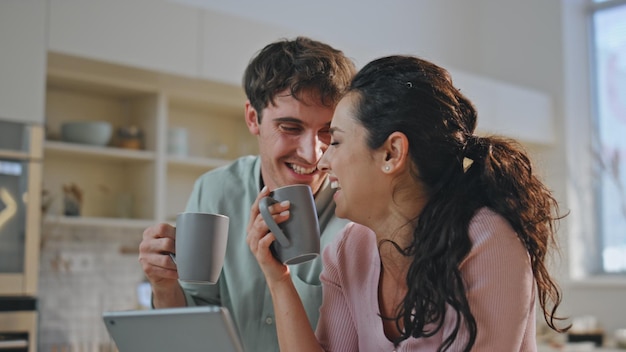 La famille boit du café, la tablette est assise, la cuisine est proche, le couple heureux rit.