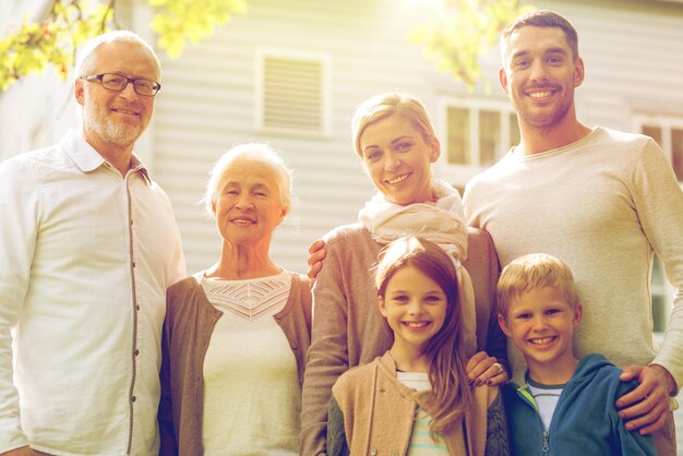 famille, bonheur, génération, maison et concept de personnes - famille heureuse debout devant la maison à l'extérieur