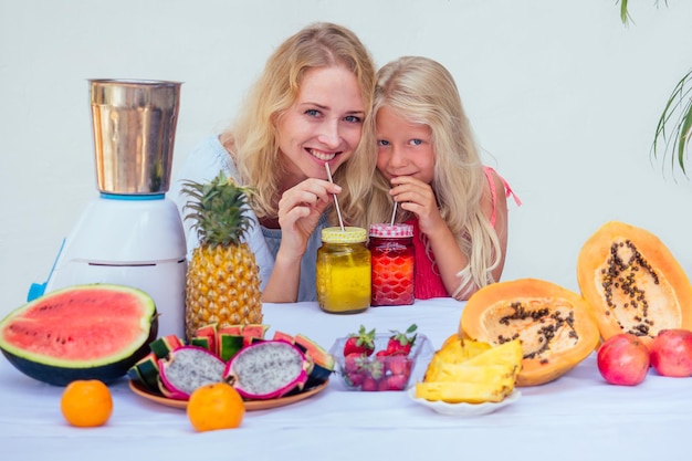 Famille caucasienne dans la cuisine pendant le petit déjeuner à la maison. deux soeurs blondes cuisinant des smoothies dans un mélangeur.thème d'été tropical