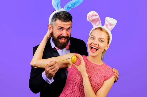 La famille célèbre pâques ensemble un couple heureux dans des oreilles de lapin peignant des œufs pour les vacances