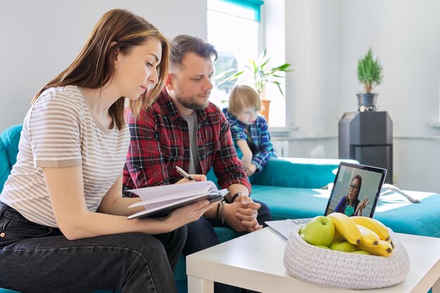 Famille de consultation médicale en ligne assise à la maison sur un canapé dans le salon avec un ordinateur portable