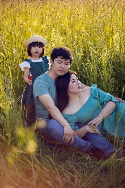 Une famille coréenne avec leur fille se trouve dans un champ dans l'herbe au coucher du soleil