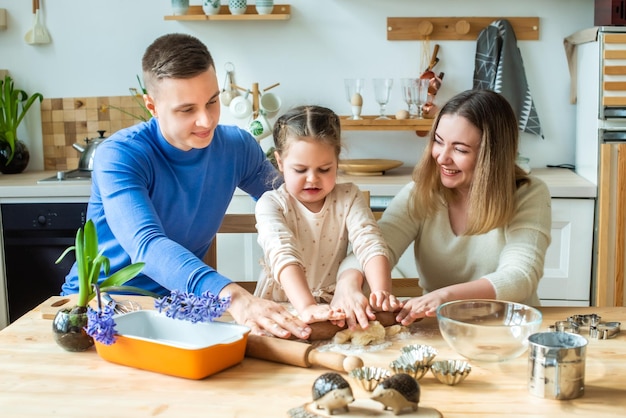 La famille cuisine à la maison maman papa et sa fille pétrissent la pâte dans une cuisine homme fille femme ensemble