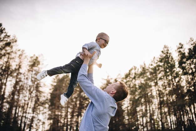 Famille dans la nature. Pique-nique en forêt, dans la prairie. L'herbe verte. Vêtements bleus. Papa, fils à lunettes. Un garçon aux cheveux blonds. Joie. Papa jette son fils en l'air. Ensemble.