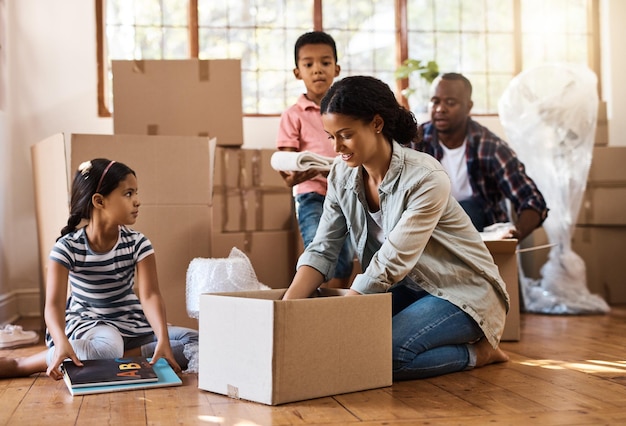 Famille déménageant et emballant des boîtes dans le salon de la maison avec les enfants maman et papa Investissement immobilier et déménagement avec quelques enfants aidant à déballer les boîtes et les cartons