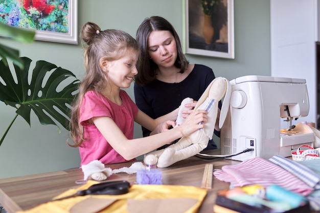 Famille, deux filles sœurs adolescentes et plus jeunes cousant ensemble un lapin de poupée jouet. Hobbies, loisirs, créativité et compétences des adolescents