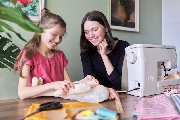 Famille, Deux Filles Sœurs Adolescentes Et Plus Jeunes Cousant Ensemble Un Lapin De Poupée Jouet. Hobbies, Loisirs, Créativité Et Compétences Des Adolescents