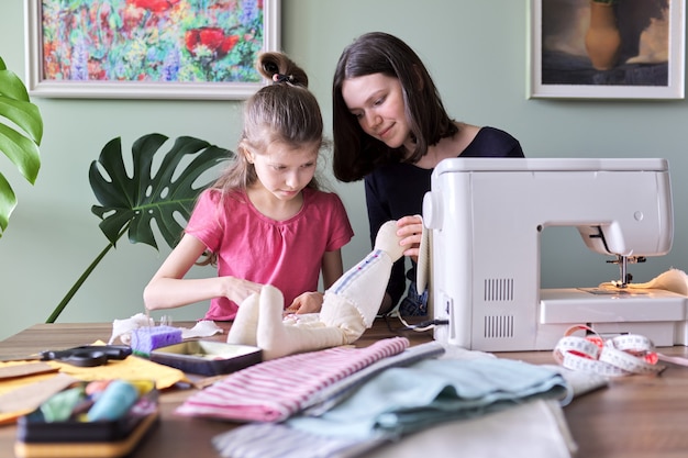 Famille, deux filles sœurs adolescentes et plus jeunes cousant ensemble un lapin de poupée jouet. Hobbies, loisirs, créativité et compétences des adolescents