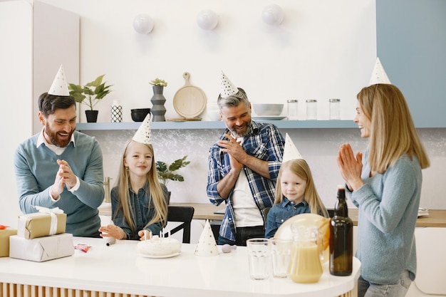 La famille et deux de leurs filles ont une célébration. Les gens applaudissent et rient. Les cadeaux sont sur la table.