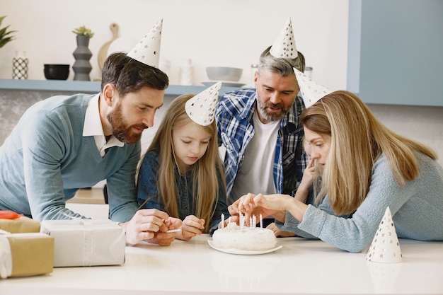 La famille et deux de leurs filles ont une célébration. Les gens regardent un gâteau avec des bougies.