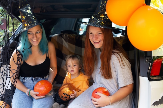 Famille diversifiée célébrant Halloween dans le coffre de la voiture. Filles s'amusant à l'extérieur en journée d'automne. Photo de haute qualité. Restez à la maison Halloween. Célébration dans l'isolement. La charité s'il-vous-plaît.