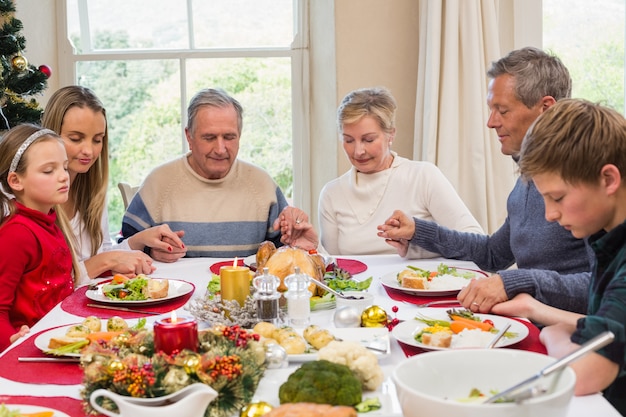 Famille élargie qui dit grâce avant le dîner de Noël