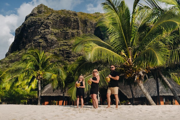 Une famille élégante en vêtements noirs avec des noix de coco à la main sur la plage de l'île MauriceBelle famille sur l'île Maurice dans l'océan Indien