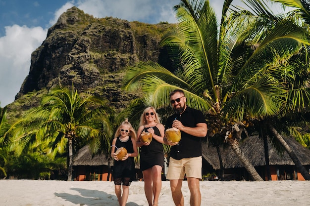 Une famille élégante en vêtements noirs avec des noix de coco à la main sur la plage de l'île MauriceBelle famille sur l'île Maurice dans l'océan Indien