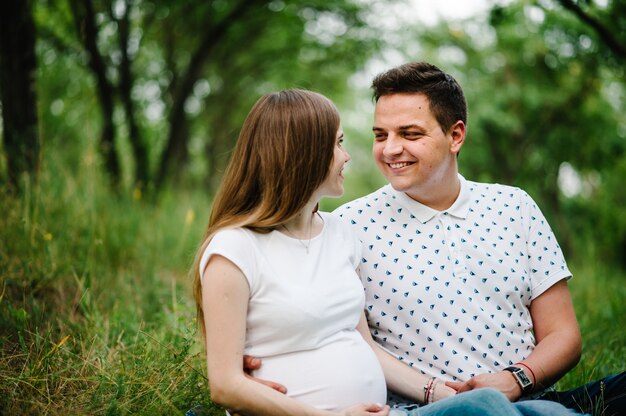 Famille enceinte assise sur l'herbe à l'extérieur dans le fond du jardin.