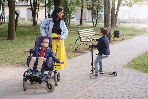 Photo famille avec un enfant atteint de paralysie cérébrale sur un fauteuil roulant spécial marchant à l'extérieur intégration