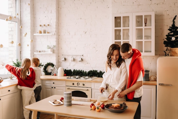 Une famille avec des enfants qui s'amusent et rient en se préparant pour les vacances de Noël dans la cuisine