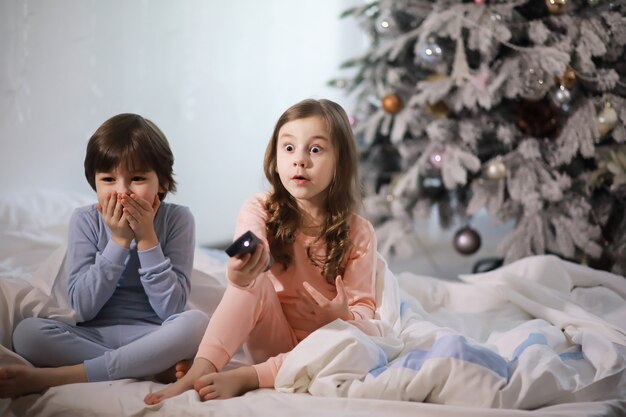 Une famille avec des enfants s'amusant sur le lit sous les couvertures pendant les vacances de Noël.