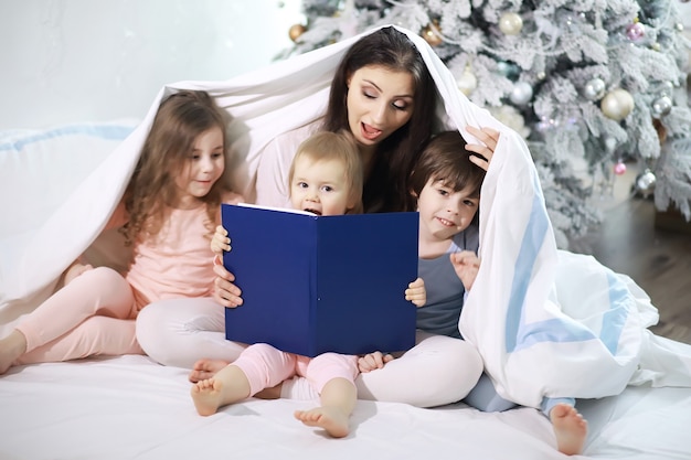 Une famille avec des enfants s'amusant sur le lit sous les couvertures pendant les vacances de Noël.