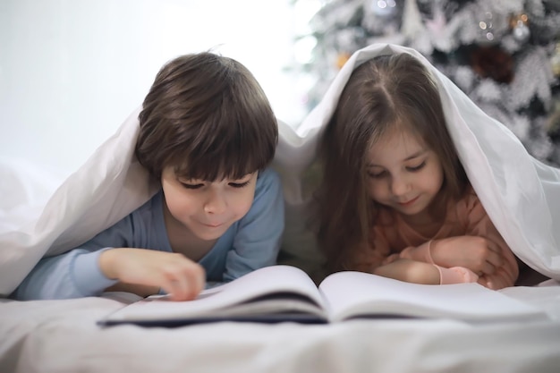 Une famille avec des enfants s'amusant sur le lit sous les couvertures pendant les vacances de Noël.