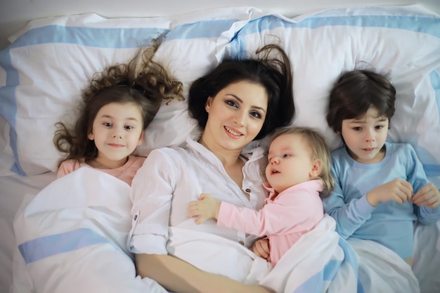 Une famille avec des enfants s'amusant sur le lit sous les couvertures pendant les vacances de Noël.