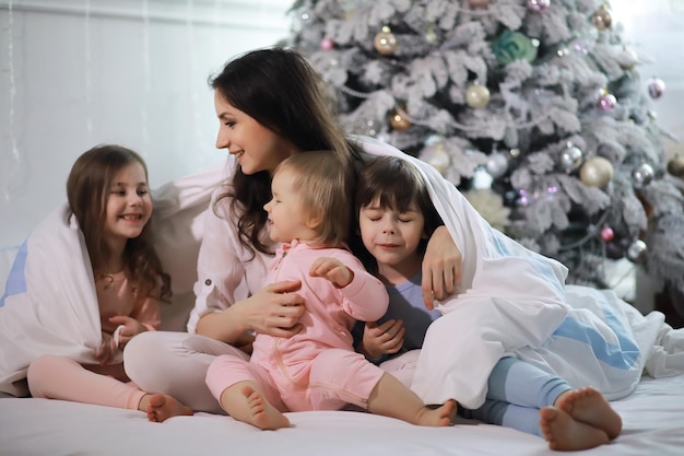 Une famille avec des enfants s'amusant sur le lit sous les couvertures pendant les vacances de Noël