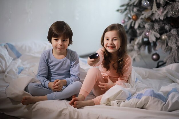 Une famille avec des enfants s'amusant sur le lit sous les couvertures pendant les vacances de Noël.