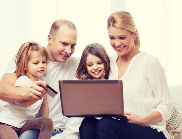 famille, enfants, technologie, argent et concept de maison - famille souriante et deux petites filles avec ordinateur portable et carte de crédit à la maison