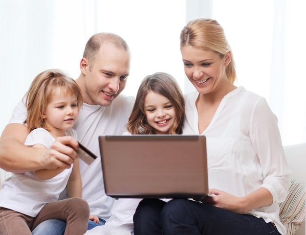 famille, enfants, technologie, argent et concept de maison - famille souriante et deux petites filles avec ordinateur portable et carte de crédit à la maison