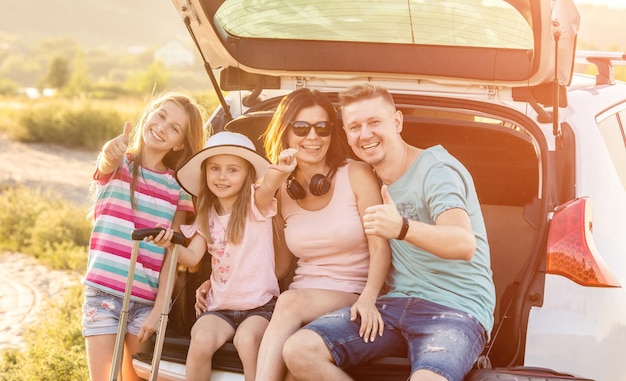 La famille est assise ensemble dans le coffre de la voiture et sourit et part en voyage