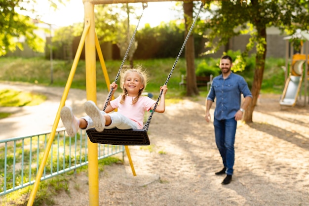 Une famille européenne heureuse de père et de fille passant du temps sur le terrain de jeu jouant et le père poussant