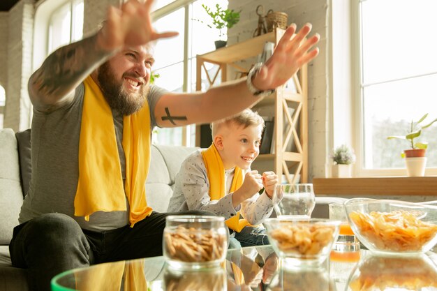 Famille excitée en regardant le football, match de sport à la maison. Père et fils à la recherche d'une chaîne de télévision avec une équipe nationale de basket-ball, football, tennis, soccer, hockey. Concept d'émotions, de soutien, d'encouragement.