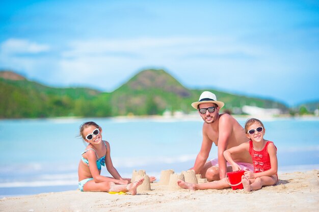 Famille Faisant Le Château De Sable à La Plage Blanche Tropicale. Père Et Deux Filles Jouant Avec Du Sable Sur Une Plage Tropicale